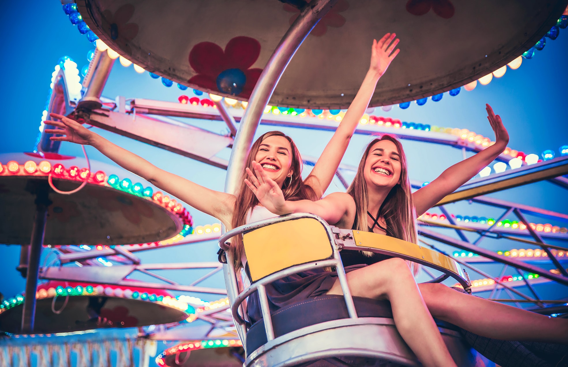 Zwei junge Frauen, sommerlich und festlich gekleidet, jubeln im Frühlingsfest-Fahrgeschäft